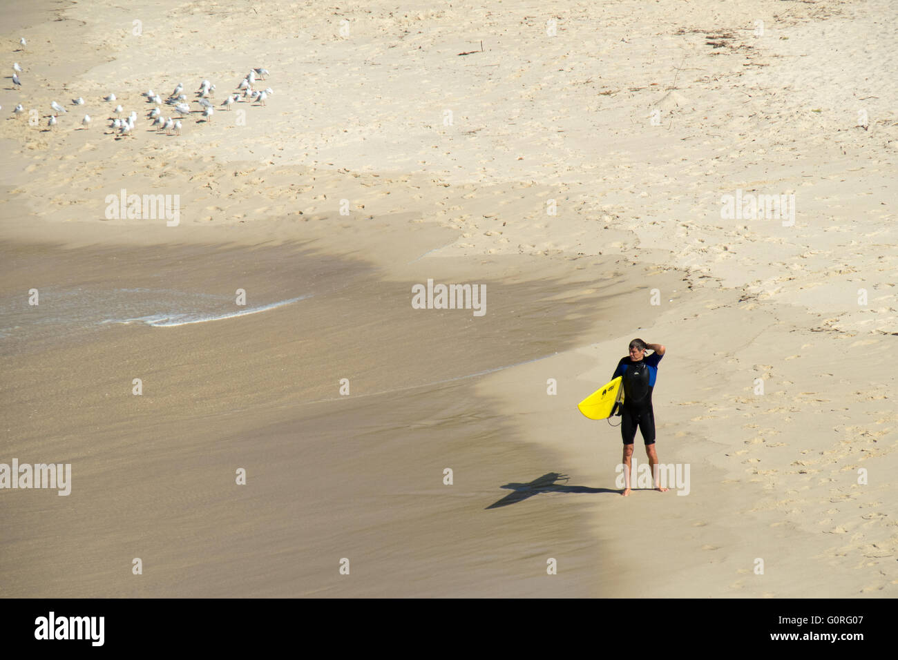 Ein einsamer Surfer mit einem gelben Surfbrett stehen am Rand des Wassers. Stockfoto