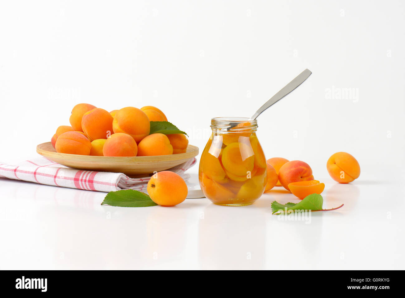 Glas mit Aprikosen-Kompott und Schüssel mit frischen Aprikosen Stockfoto