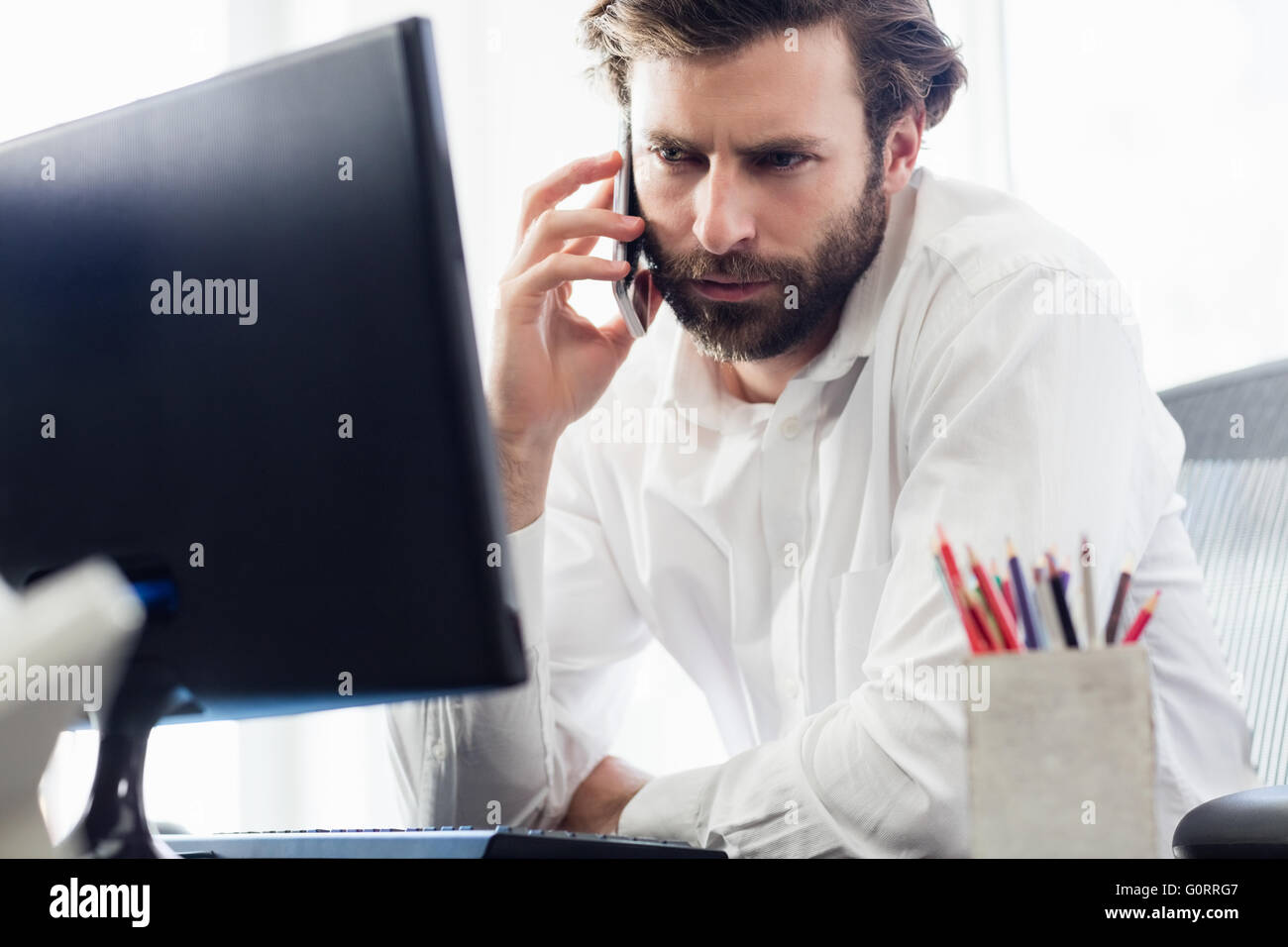 Ein Mann vorbei einen Anruf vor seinem computer Stockfoto