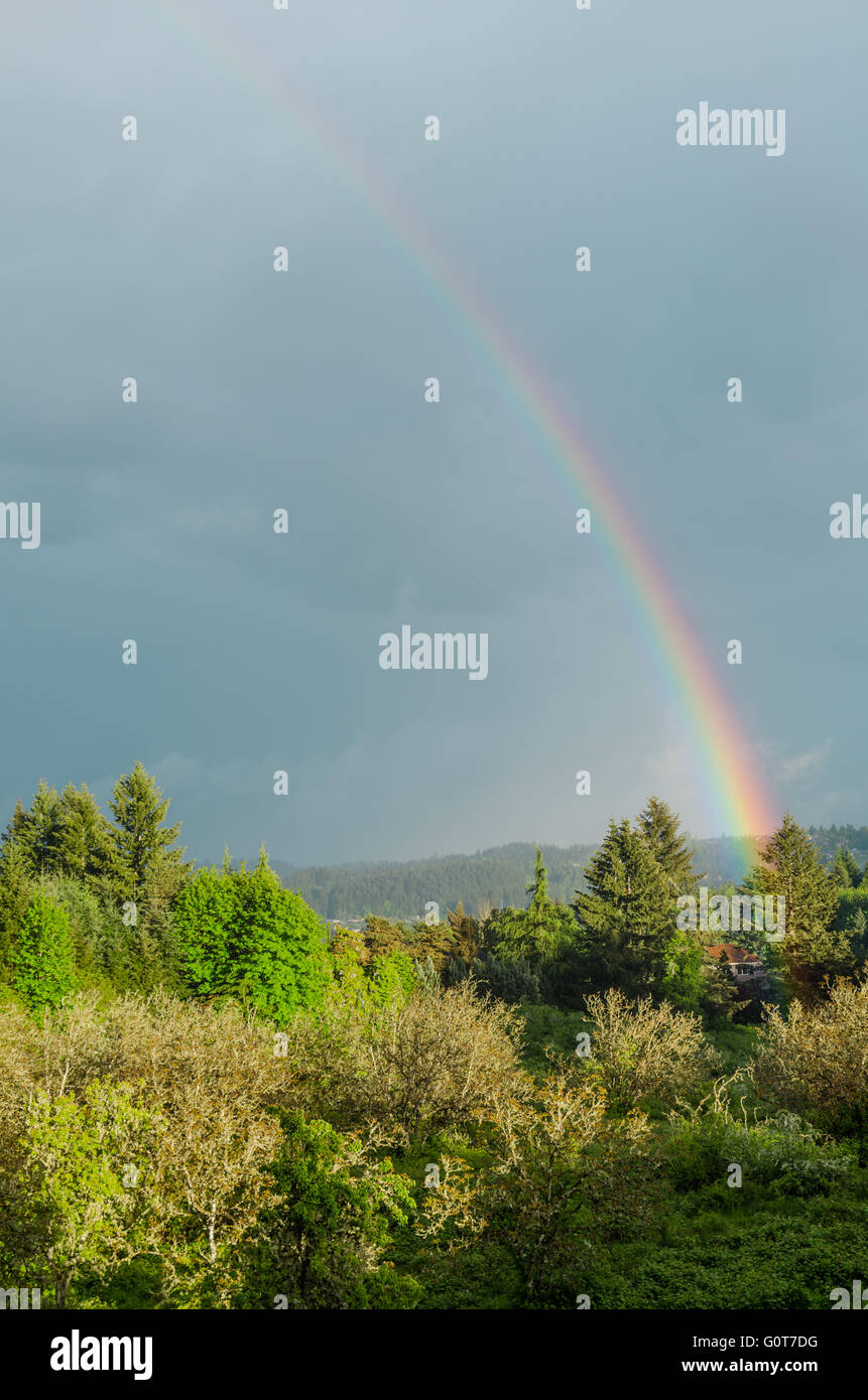 Ein Regenbogen erstreckt sich über einen blauen Himmel und Erde in der Nähe ein Bauernhaus und Wiese berührt. Stockfoto
