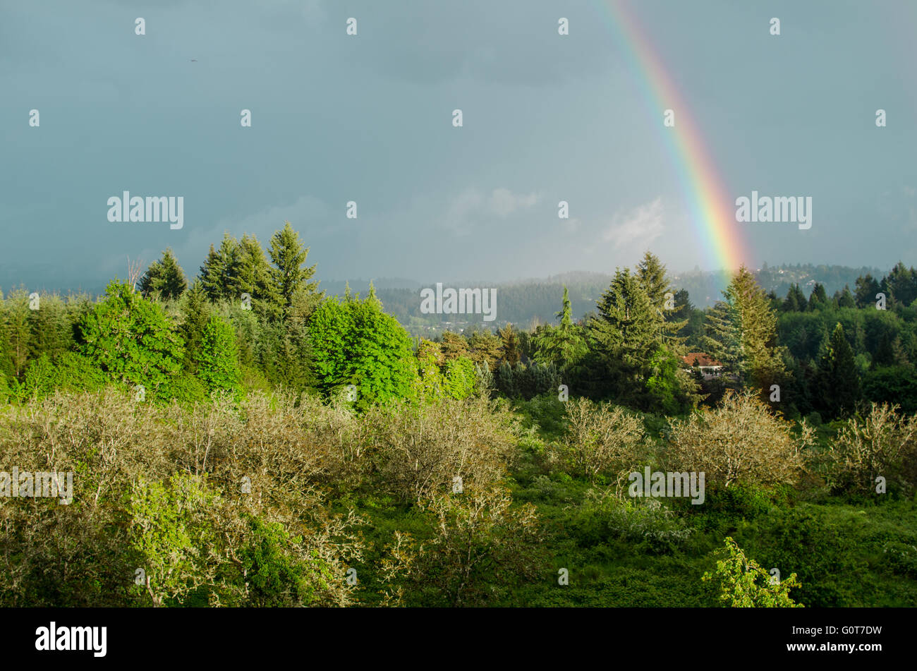 Ein Regenbogen erstreckt sich über einen blauen Himmel und Erde in der Nähe ein Bauernhaus und Wiese berührt. Stockfoto