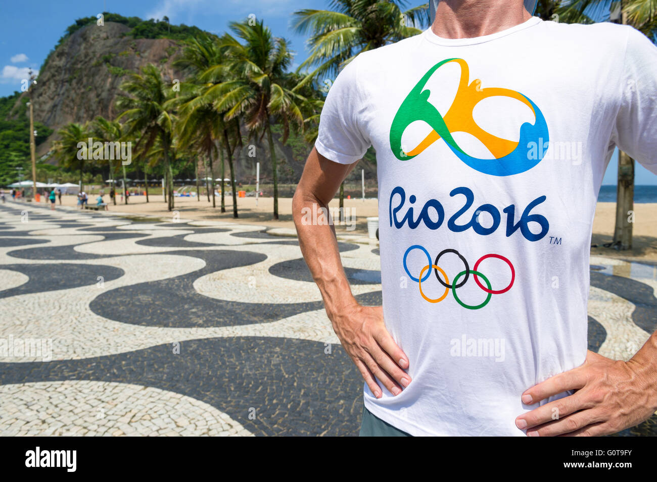 RIO DE JANEIRO - 10. März 2016: Mann mit offiziellen steht Rio 2016 T-shirt auf dem Bürgersteig Copacabana Strand. Stockfoto