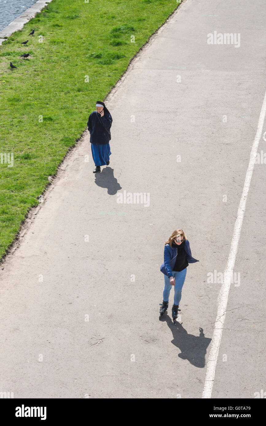 Junge Frau Alte Frau, Ansicht einer jungen Frau auf Rollschussen, die an einer Nonne auf dem Rybaki-Weg entlang der Weichsel in Krakau, Polen, vorbeikommt. Stockfoto