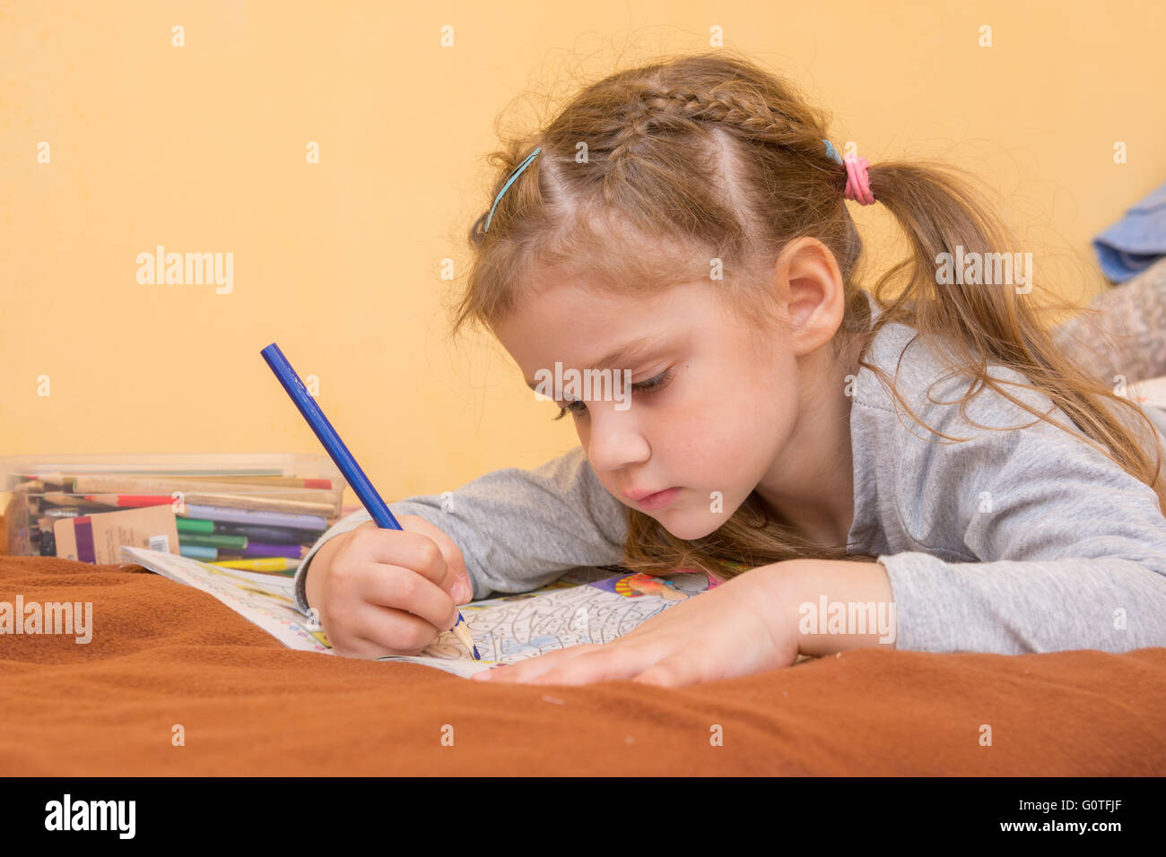 Kleines Mädchen zieht eine harte liegend auf dem Bauch mit einem Bleistift auf Papier Stockfoto