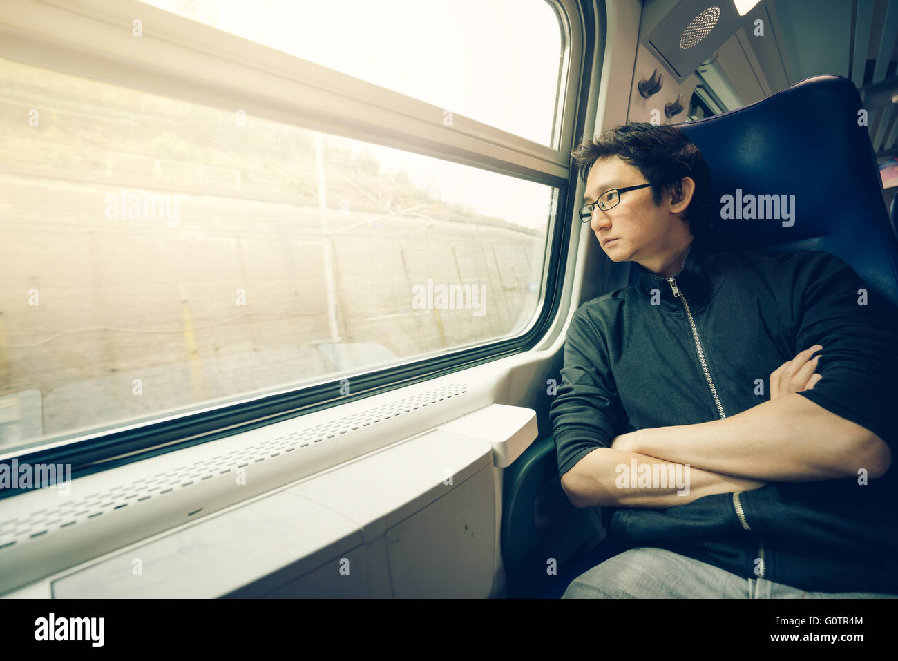 Schöner asiatischer Mann Blick durch Zugfenster, leichten Warmton mit Textfreiraum Stockfoto