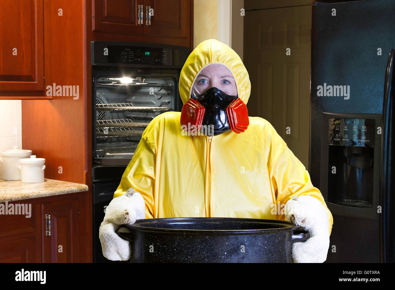 Frau in gelb Schutzanzug und Atemschutzmaske Holding Bräter in Küche. Stockfoto