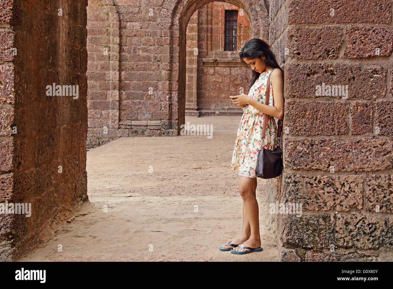 Jung, ernst Mädchen beschäftigt mit Smartphone lehnte sich gegen den Bogen Wand in einem alten Backsteingebäude. Stockfoto