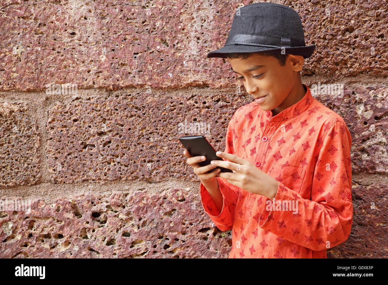 Nahaufnahme von glücklich teenboy mit schwarzen Hut mit Smartphone, roten Ziegelmauer gelehnt Stockfoto