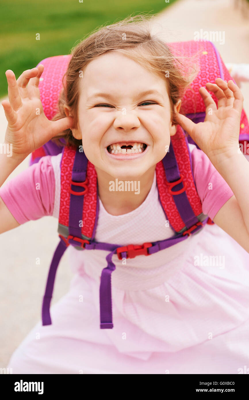 Porträt von 5 Jahre altes Mädchen mit rosa und lila Schultasche, Grimassen und Blick in die Kamera, zeigen ihre vorderen Zähne fehlen Stockfoto