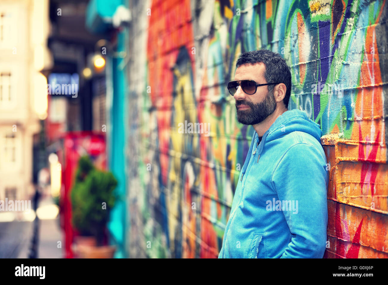 Gut aussehender Mann mit stilvollen Sonnenbrille, Stand in der Nähe schöne bunte Wand auf der Straße, urban Fashion-Look, Leben in der Stadt Stockfoto