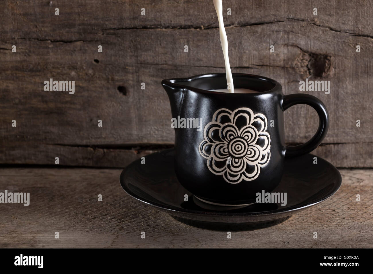 Füllen Sie Milch in eine schwarze Tasse auf alten Holztisch Stockfoto