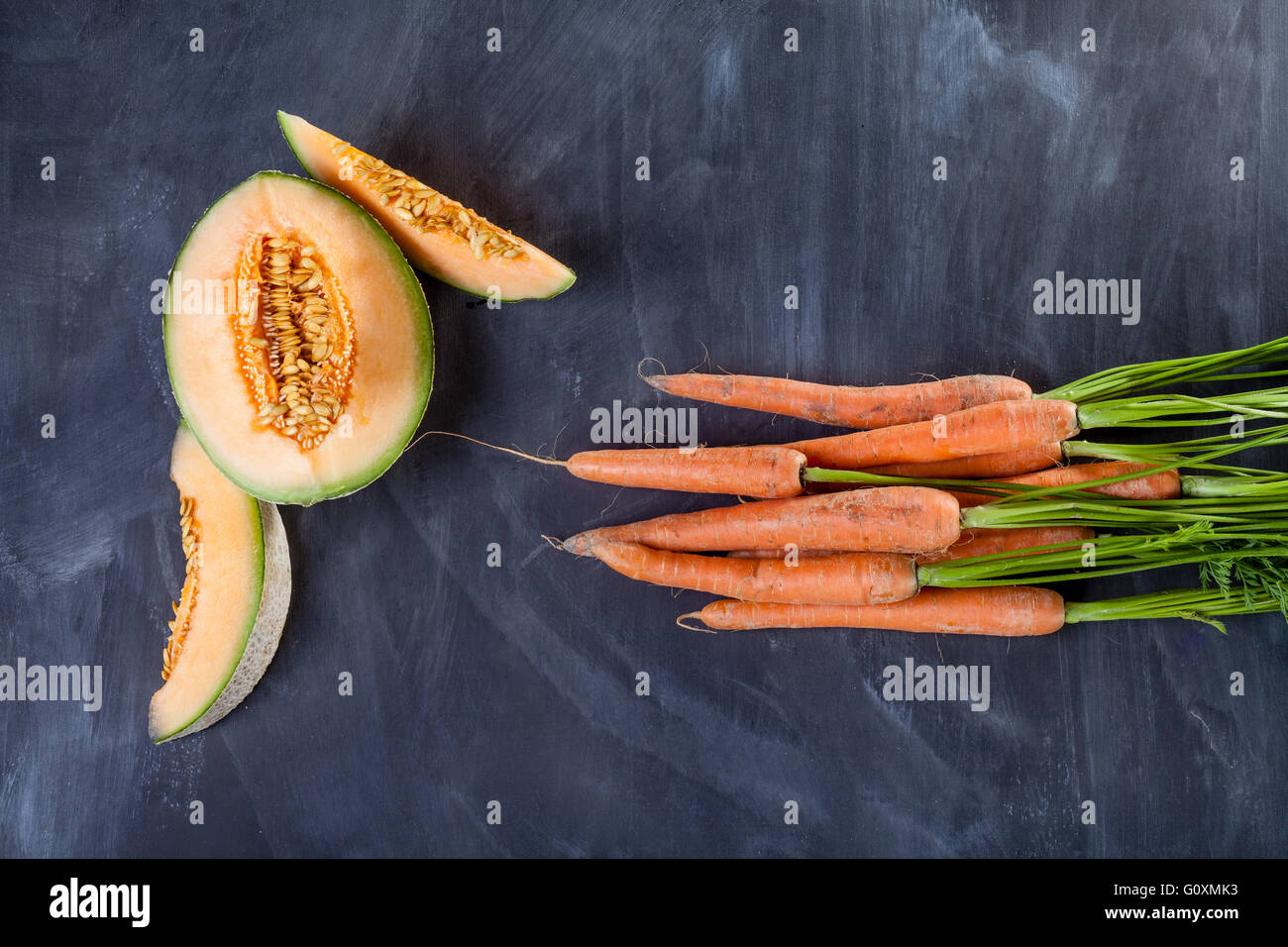 Scheiben von Melone und Haufen von Karotten am schwarzen Brett Stockfoto