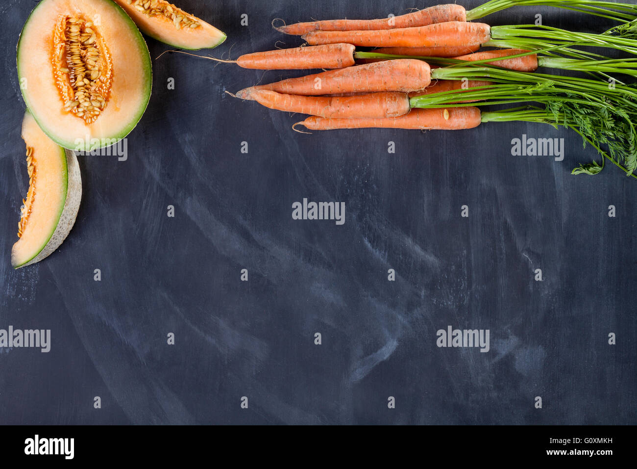 Scheiben von Melone und Haufen von Karotten am schwarzen Brett von oben Stockfoto