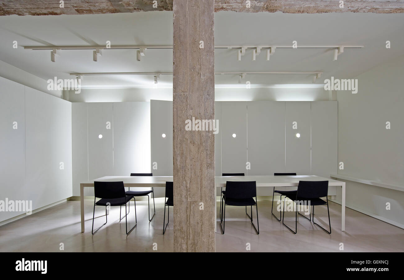 Langer Tisch mit Stühlen in modernen weißen Raum mit Deckenstrahler und Holz Säule. Stockfoto