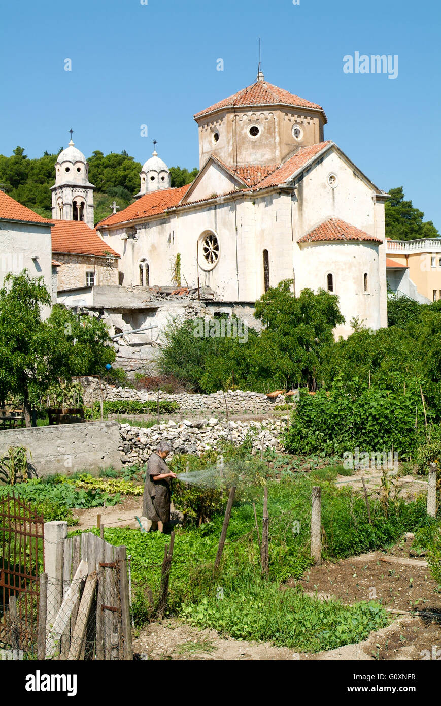 Skradin, Kroatien - 26. August 2004: Frau Bewässerung ihres Gartens vor der Kirche in Skradin in Kroatien Stockfoto