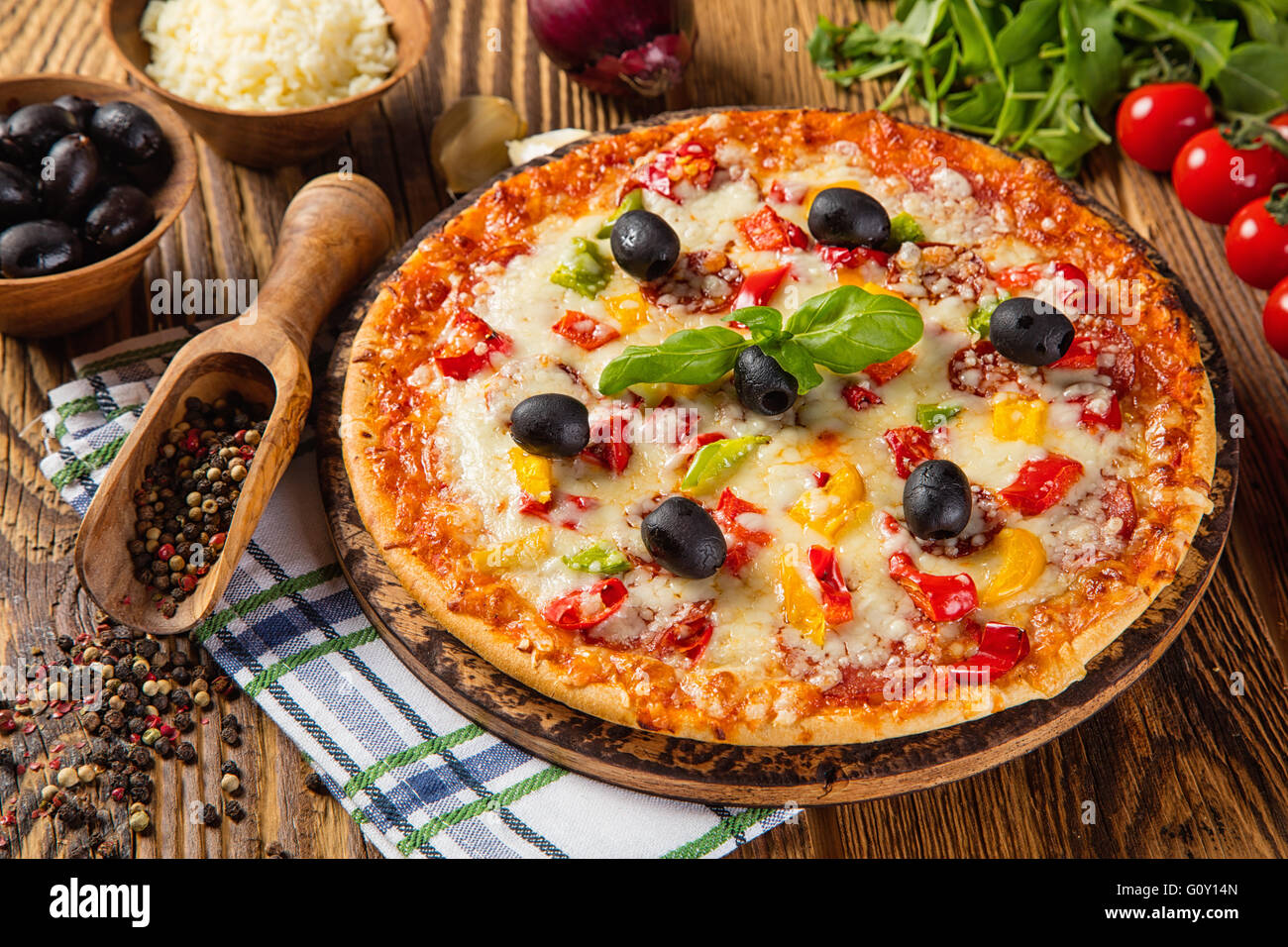 Rustikale Pizza mit Mozzarella, Schinken, Oliven und Basilikum. Serviert auf Vintage Holztisch Stockfoto
