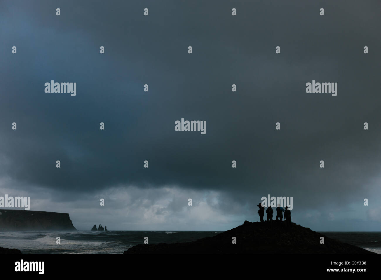 Silhouetten von 4 Touristen betrachten die Felsformationen des Vik, Island an einem stürmischen Tag Stockfoto