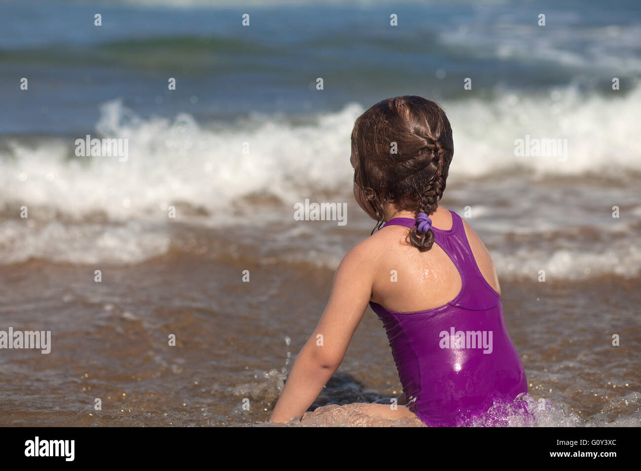 Rückansicht des Mädchen sitzen am Strand am Wasserrand Stockfoto