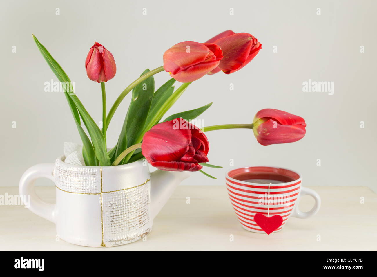 Rote Tulpen mit einer Tasse Tee auf einem Holztisch Stockfoto