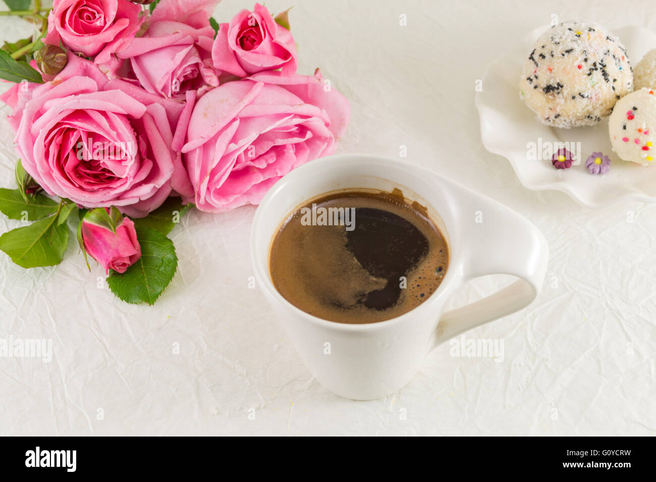 Rosa Rosen und eine Kaffeetasse auf weiße Seide Textil Stockfoto