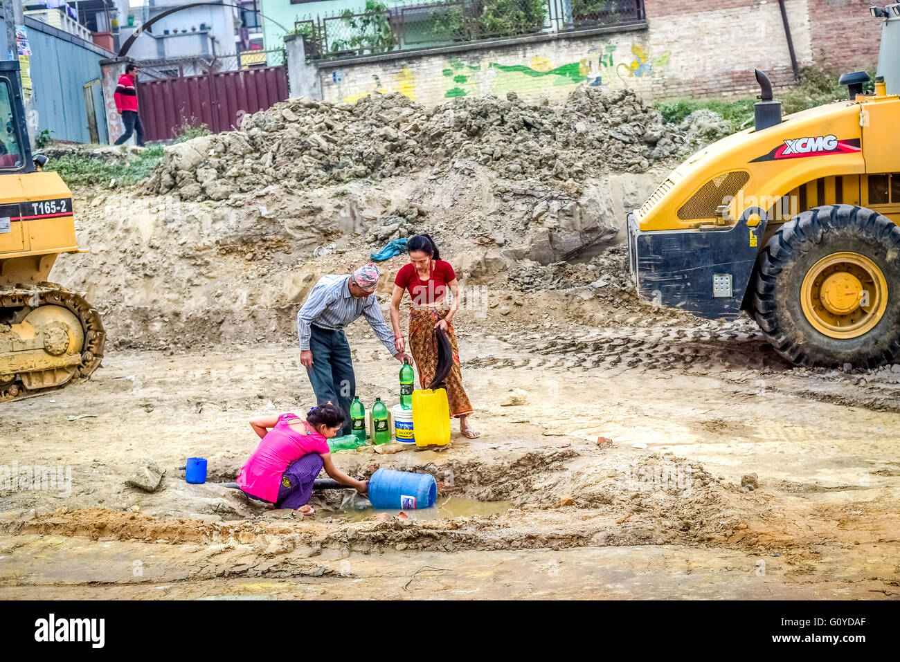 Eine einheimische Familie nimmt Wasser aus einer kaputten Wasserleitung während der Trockenzeit in Kathmandu, ein Jahr nach den Erdbeben in Nepal 2015. Stockfoto