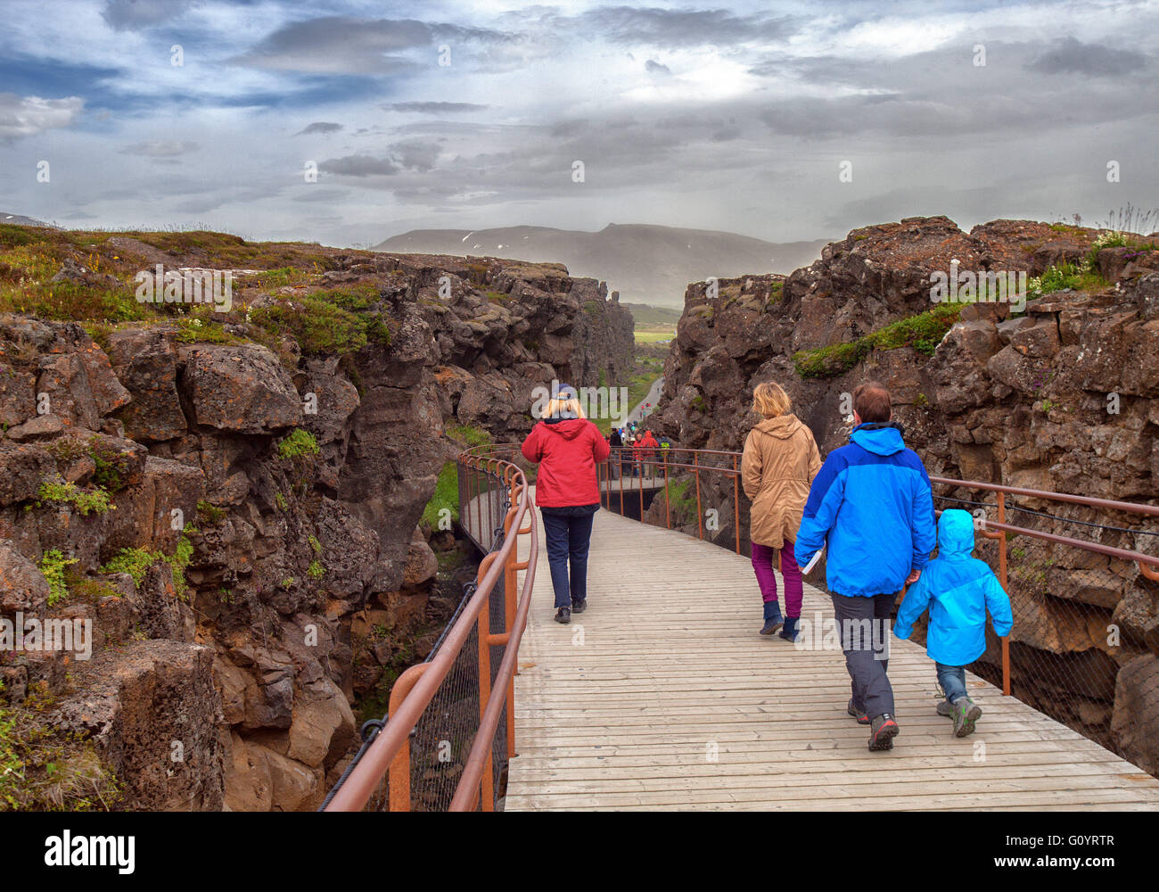 Süd-West Island, Island. 4. August 2015. Touristen gehen auf eine Brücke Weg zwischen Mauern aus vulkanischem Gestein durch berühmte Almannagja Canyon im Thingvellir National Park, ein Grabenbruch markieren das Wappen des Mittelatlantischen Rückens zwischen den nordamerikanischen und eurasischen Platten, es ist eine visuelle Darstellung der Kontinentalverschiebung, die zwischen zwei tektonischen Platten gebildet. Es ist eine der meistbesuchten Touristenattraktionen in Island, wo Tourismus ein wachsender Sektor der Wirtschaft geworden. Touristen gehen auf eine Brücke Weg zwischen Mauern aus vulkanischem Gestein durch berühmte Almannagja Canyon in Thingvellir National Stockfoto