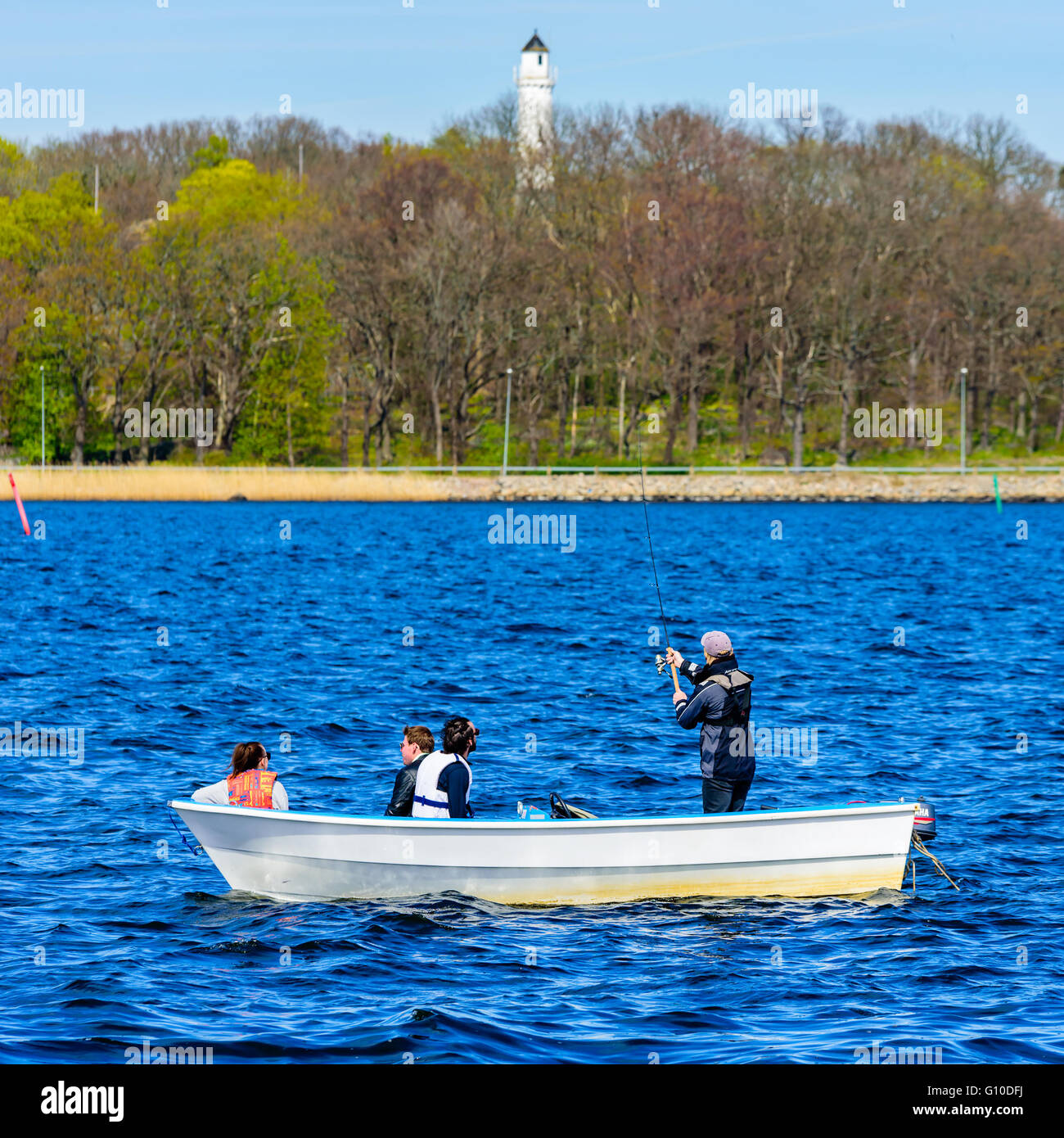 Karlskrona, Schweden - 3. Mai 2016: Vier Personen in einem kleinen offenen Motorboot Angeln auf dem Meer Küste mit Leuchtturm in backgr Stockfoto
