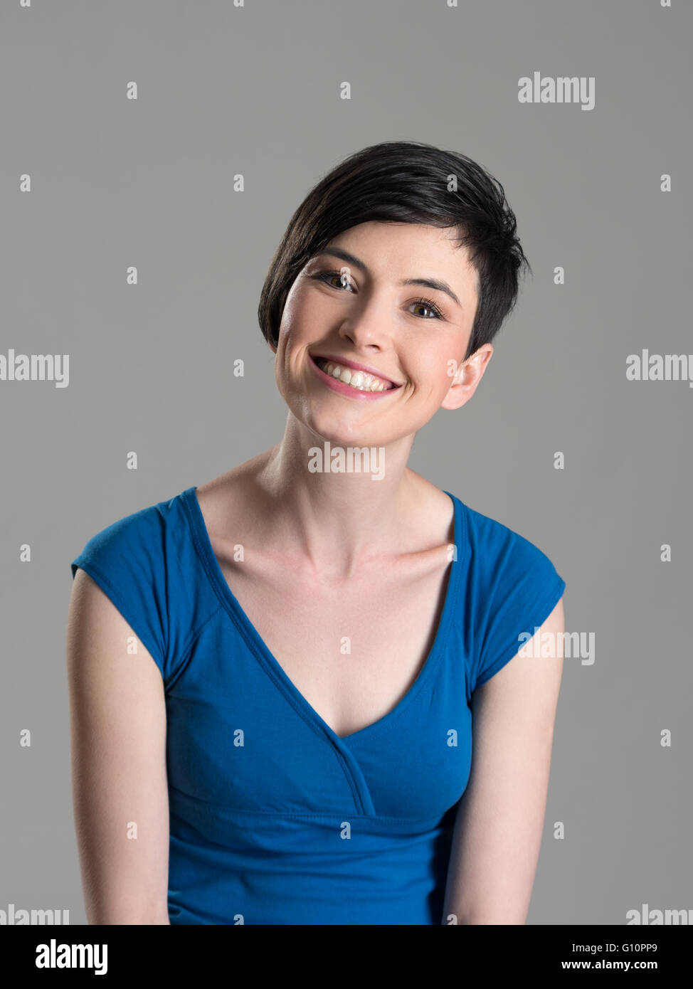 Studioportrait von niedlich schöne kurze Haare Brünette Schönheit lächelnd in die Kamera mit leicht geneigtem Kopf auf grauem Hintergrund Stockfoto