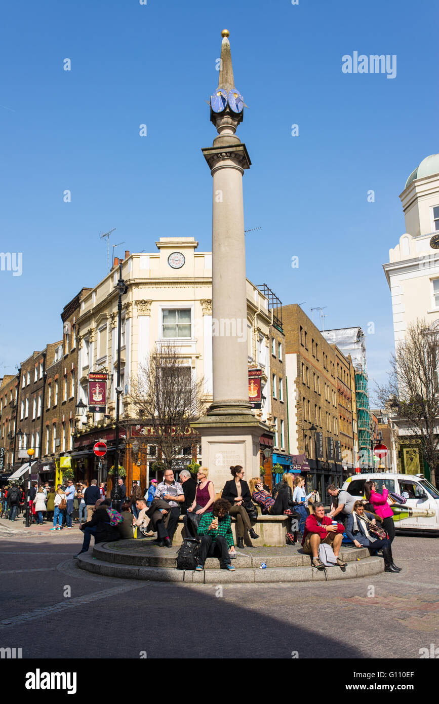 Londoner genießen die Sonne sitzen unter der Sonnenuhr Säule in Seven Dials, eine kleine Kreuzung in Covent Garden in London Stockfoto