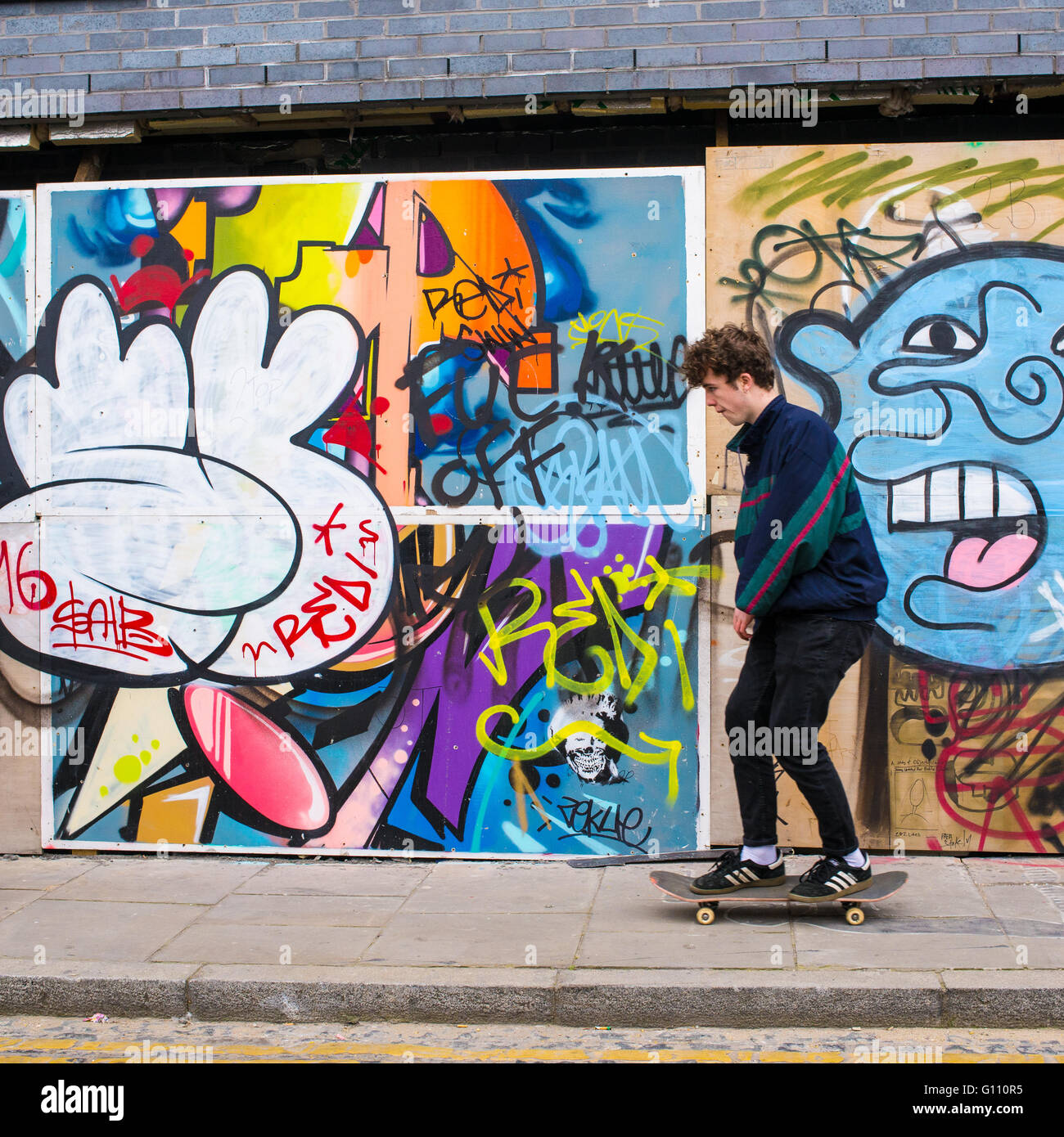 Teenager Reiten eine Skateboard auf dem Bürgersteig vor einer Wand mit einem Graffiti und Wandbilder Stockfoto