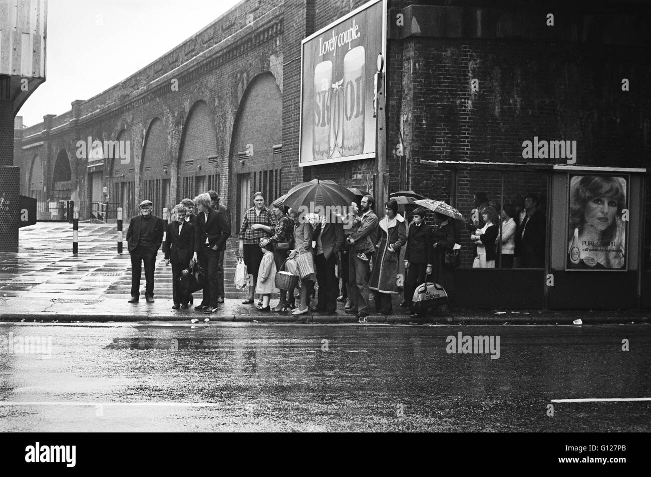 Archiv Bild eines Bus-Warteschlange in Lambeth, London, England 1979, unter einem skol Bier Reklametafeln Stockfoto