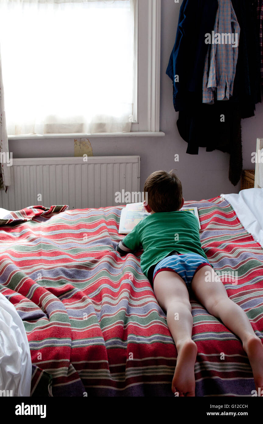 kleiner Junge liest auf dem Bett Stockfoto