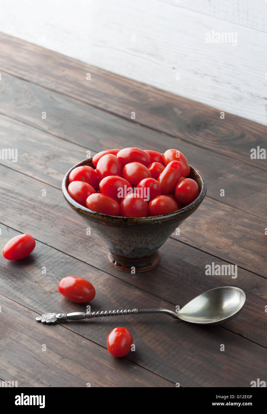 Cherry Tomaten Roma in Keramikschale auf Holztisch mit Vintage Löffel. Vertikales Bild mit Textfreiraum. Stockfoto