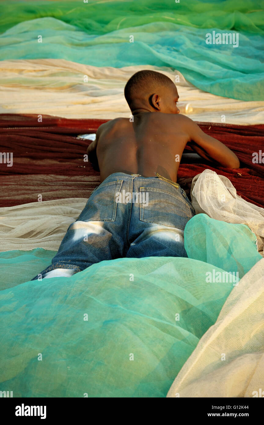 Junger Mann liegend auf dem Bauch auf bunten Fischernetze am Strand von Chembe, Cape Maclear, Malawi zum Trocknen Stockfoto