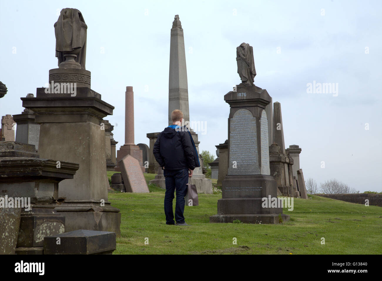 junger Mann steht jeweils vor Grabstein in der Nekropole von Glasgow, Schottland, Großbritannien Stockfoto