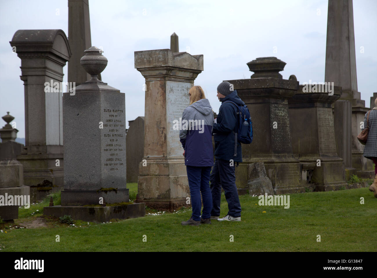 junger Mann und Frau steht jeweils vor Grabstein in der Nekropole von Glasgow, Schottland, Großbritannien Stockfoto