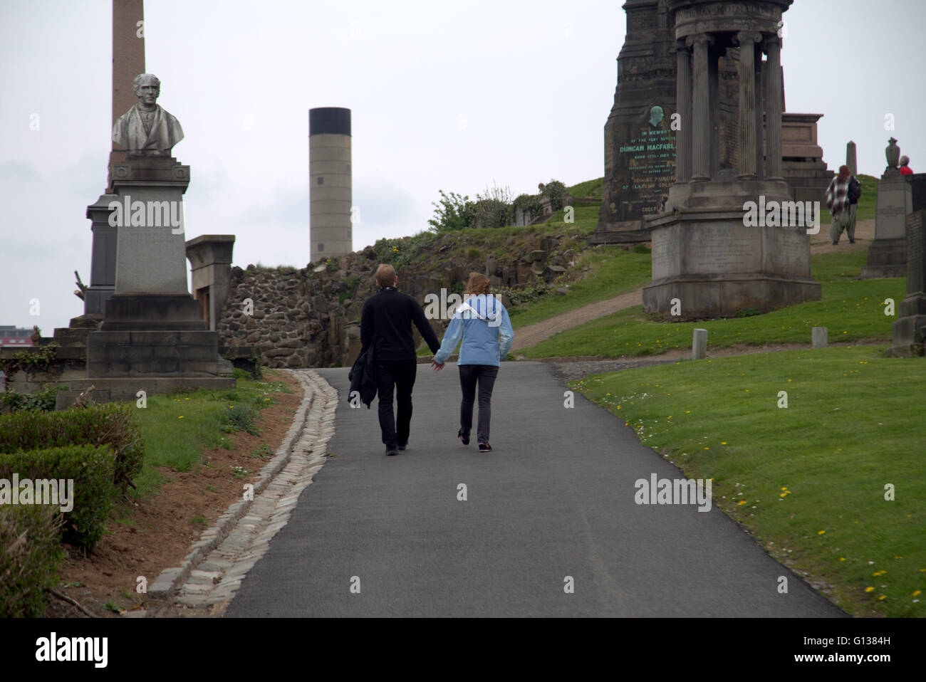 Mann und Frau gehen Hand in Hand steht jeweils vor Grab Stein in der Nekropole von Glasgow, Schottland, Großbritannien Stockfoto