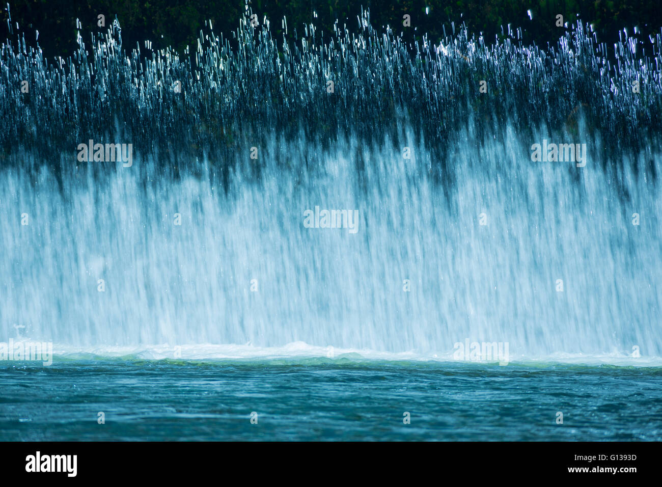 VORHANG VON FRISCHEM WASSER-KASKADEN ÜBER HOCHWASSERENTLASTUNG IN RUHIGEN POOL AM FLÜSSCHEN Stockfoto