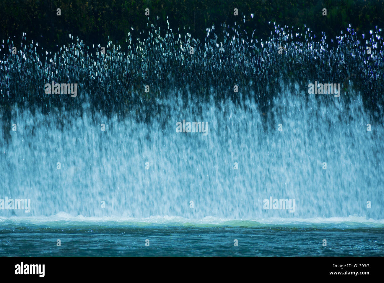VORHANG VON FRISCHEM WASSER-KASKADEN ÜBER HOCHWASSERENTLASTUNG IN RUHIGEN POOL AM FLÜSSCHEN Stockfoto