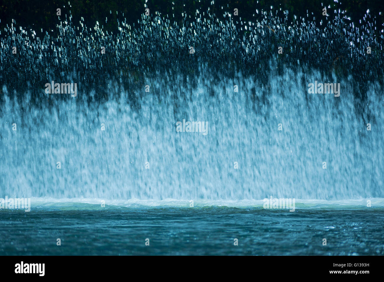 VORHANG VON FRISCHEM WASSER-KASKADEN ÜBER HOCHWASSERENTLASTUNG IN RUHIGEN POOL AM FLÜSSCHEN Stockfoto
