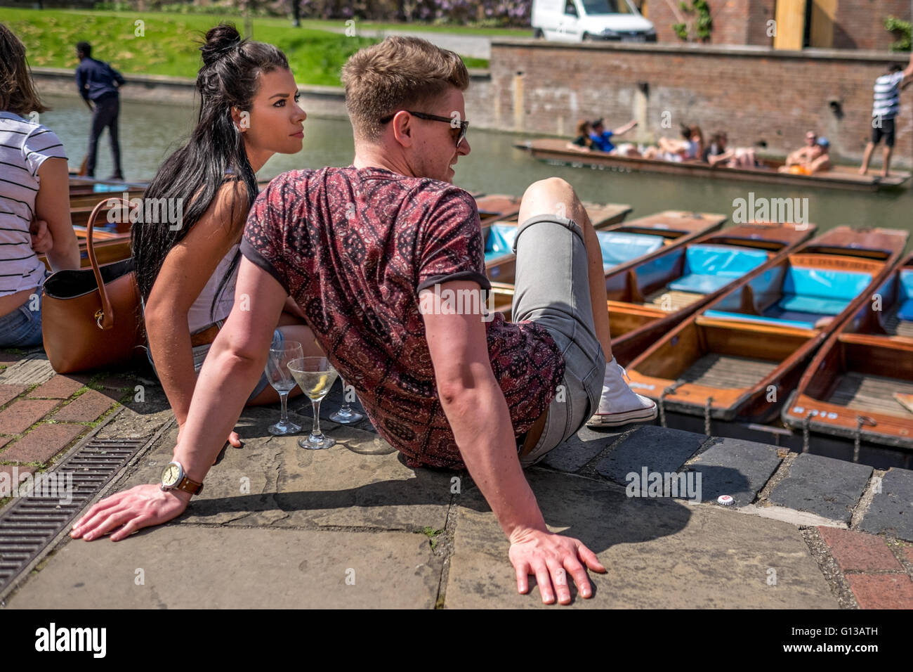 Ein schönes Paar sitzt am Ufer des Flusses Cam in der Nähe von Kai Pier an einem warmen und sonnigen Tag im Mai.  Cambridge punt Stechkahn fahren Stockfoto