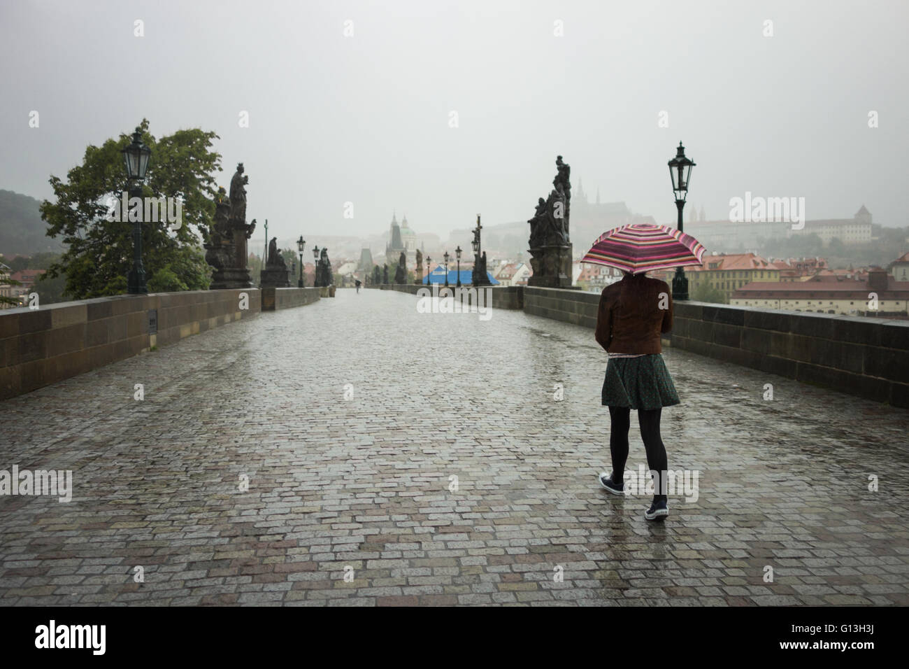 junge Frau, die zu Fuß über eine fast leere Karlsbrücke, Prag am frühen Morgen Regen Stockfoto
