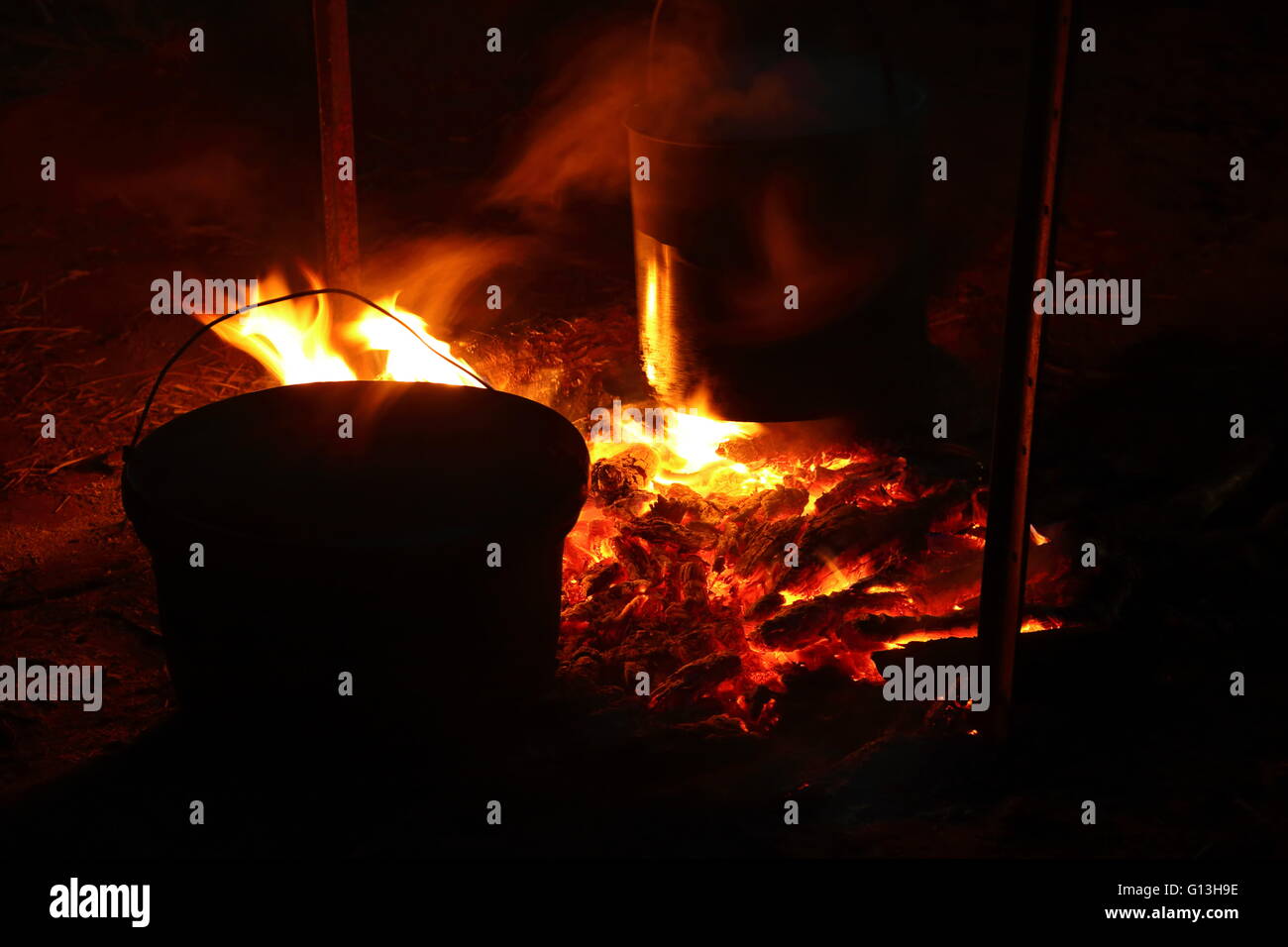 Heißen Sie Kohlen in Flammen in einem Lagerfeuer in der Nacht wie Wasser in großen Metall-Töpfen kocht Stockfoto