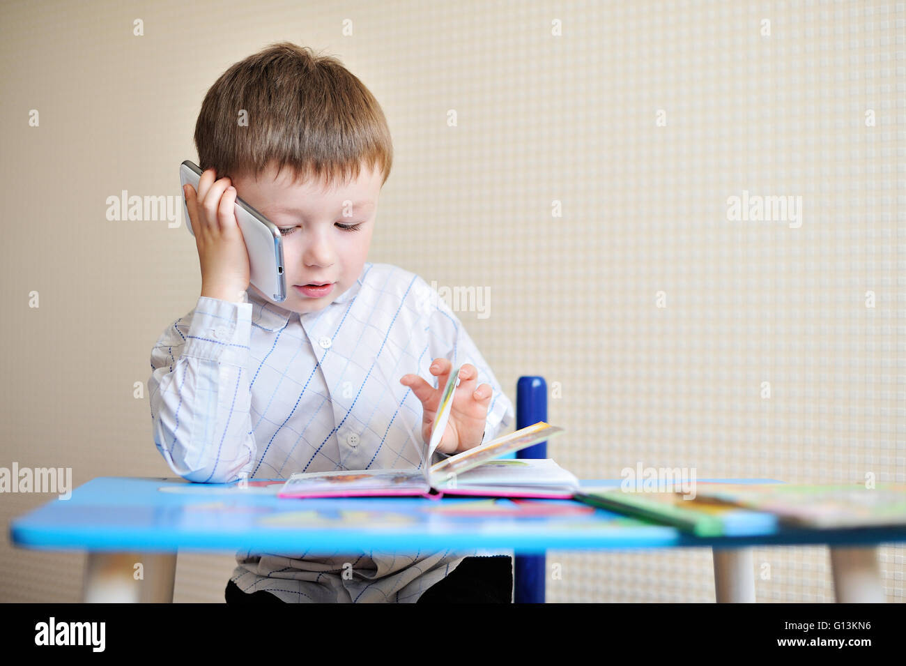 kleiner Junge sitzt an einem Schreibtisch in der Schule und sprechen am Telefon Stockfoto