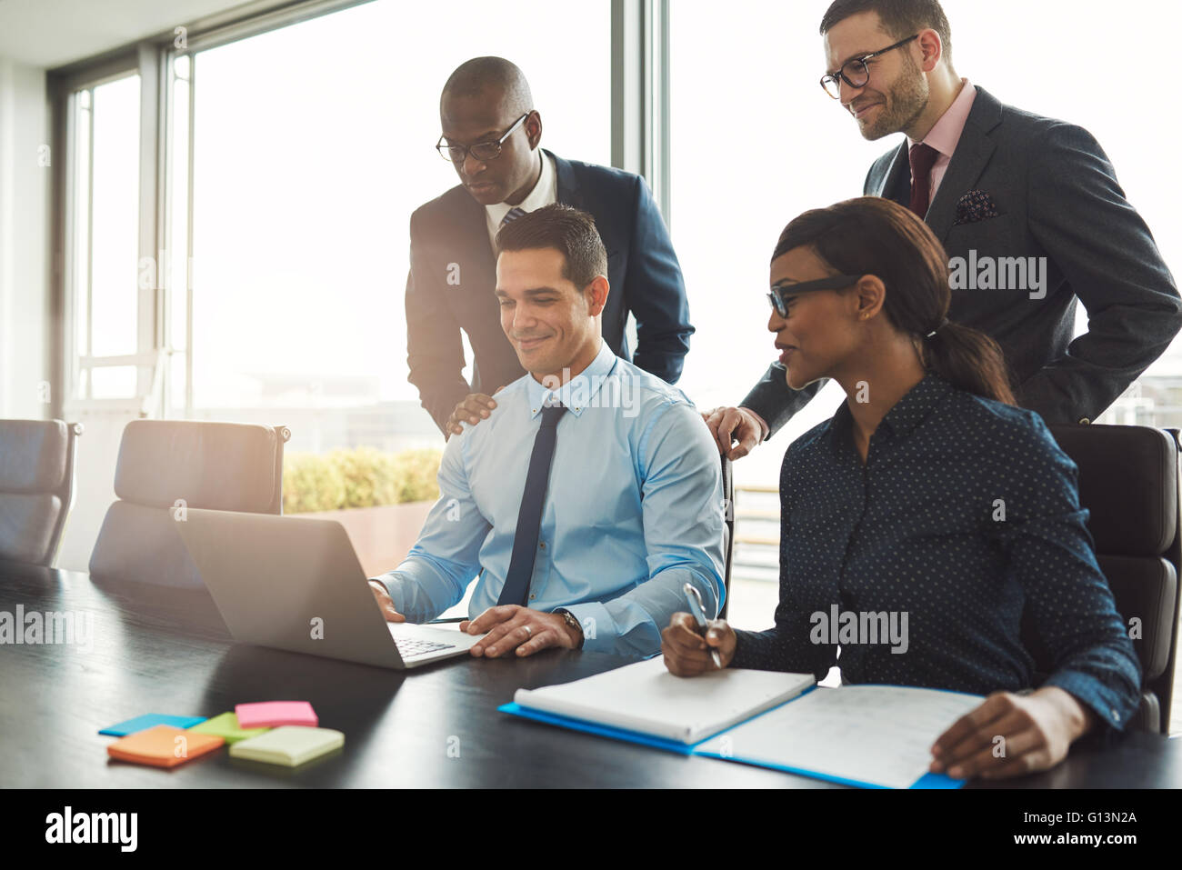 Gruppe von glücklich unterschiedlichen männlichen und weiblichen Geschäftsleuten in formalen versammelten sich um Laptop-Computer in helles Büro Stockfoto