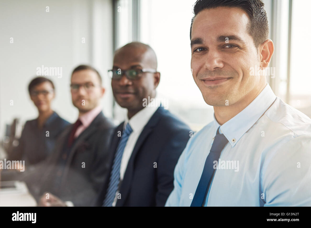 Heterogene Gruppe von vier grinsenden attraktive Business-Menschen sitzen am Tisch mit Rücken zur großen hellen Bürofenster mit leichten fl Stockfoto