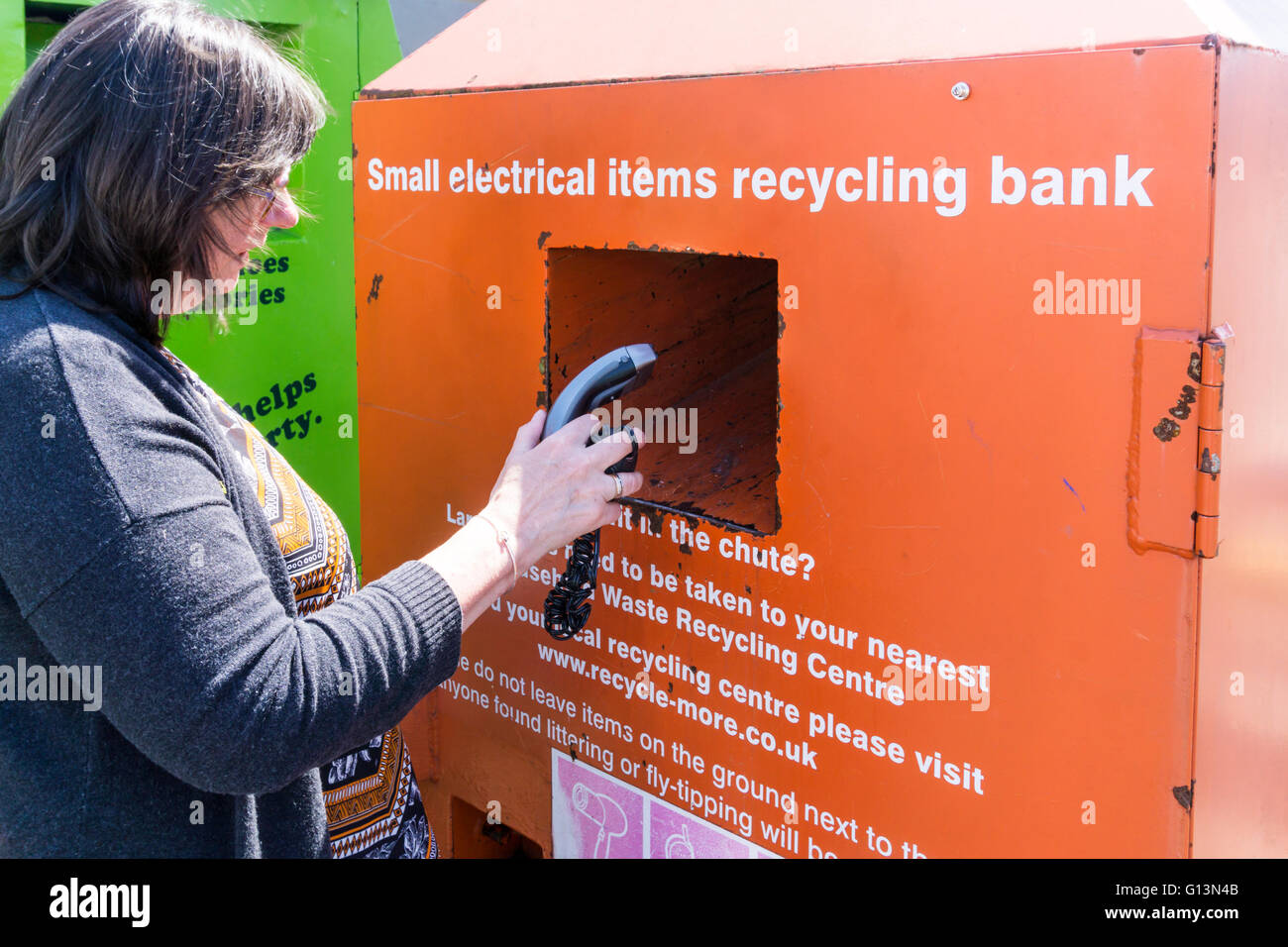 Eine Frau legt einen unerwünschten elektrischen Rasierapparat in eine kleine elektrische Geräte recycling Bank. Stockfoto