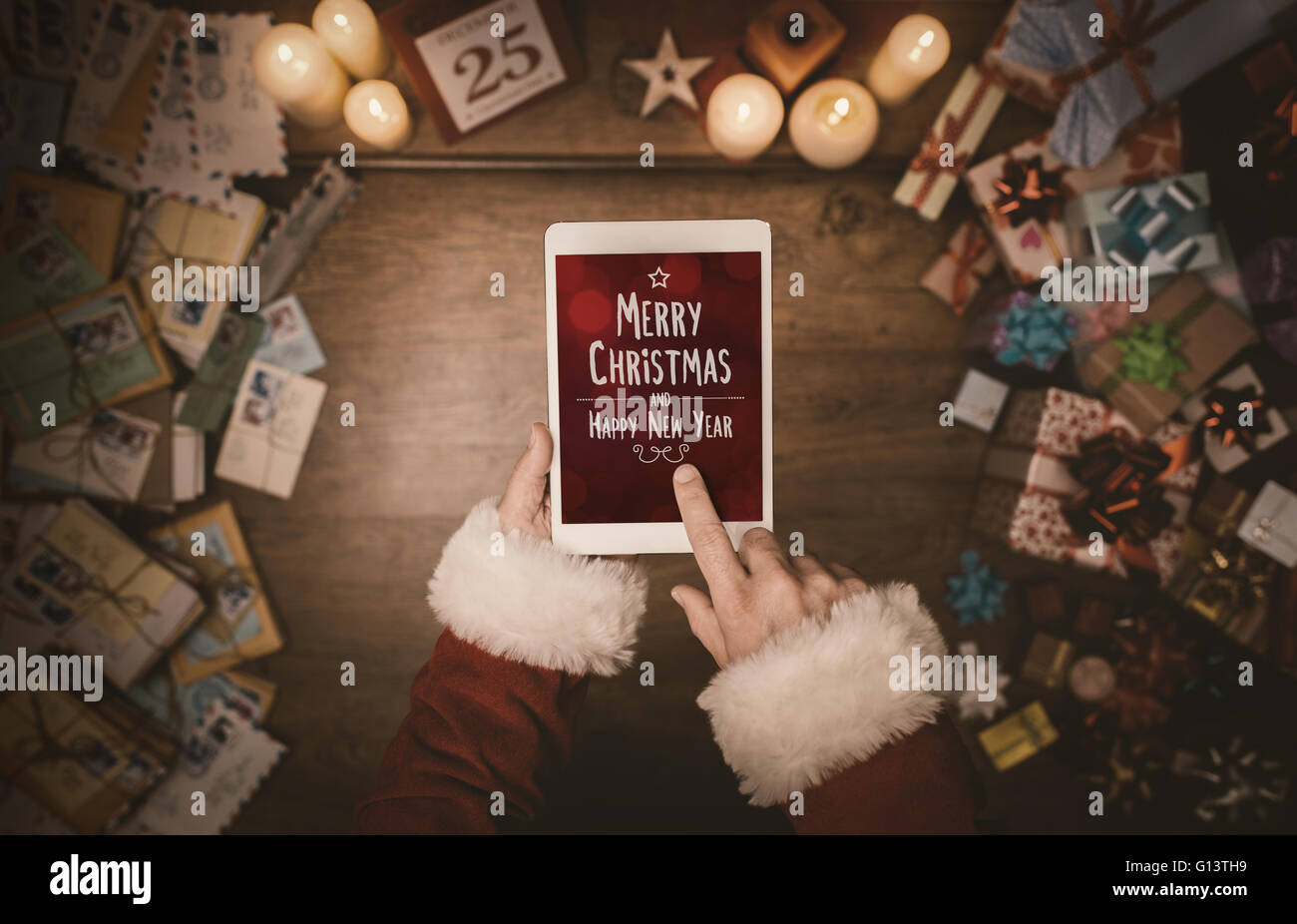 Santa Claus mit digital Touch-Screen-Tablette, Hände nah oben, Ansicht von oben, Desktop mit Buchstaben und Weihnachtsgeschenke Stockfoto