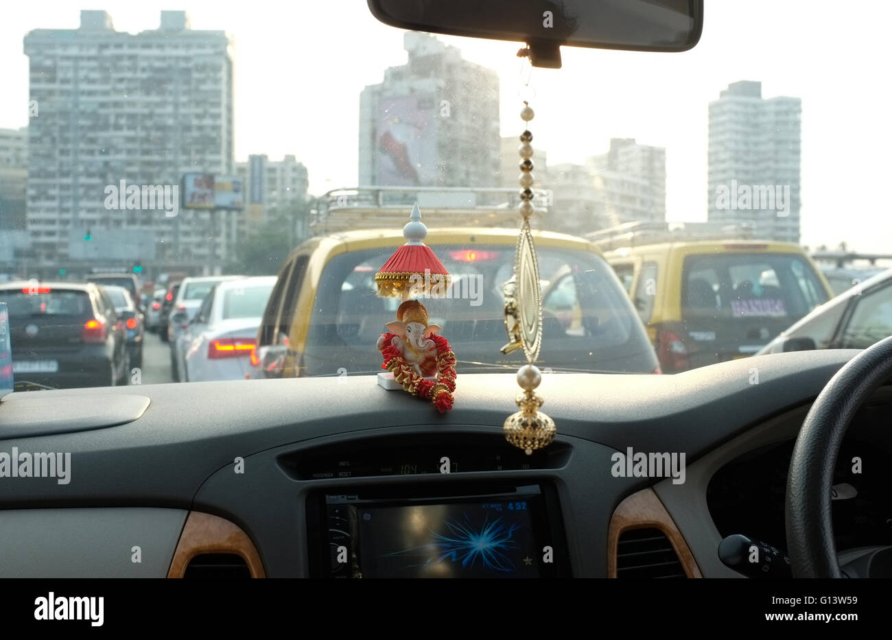 Blick aus einem Auto, das durch viel Verkehr in Mumbai, Indien. Glücksbringer auf dem Armaturenbrett aus Spiegel hängen Stockfoto