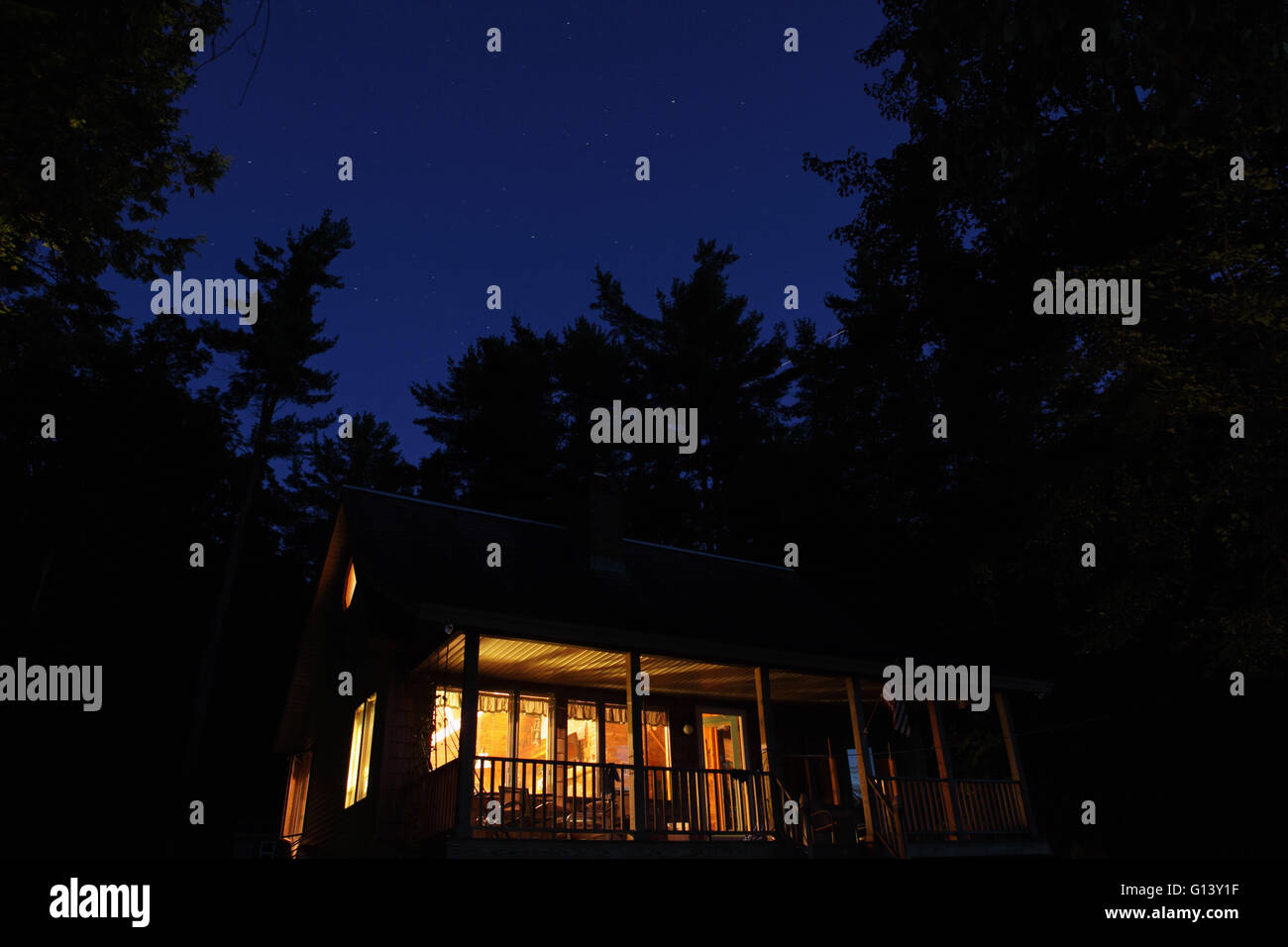 Kabine leuchtet im Wald an einem See im westlichen Vermont, USA, in der Nacht mit einem Sternenhimmel und die Raumstation ISS vorbei in eine l Stockfoto